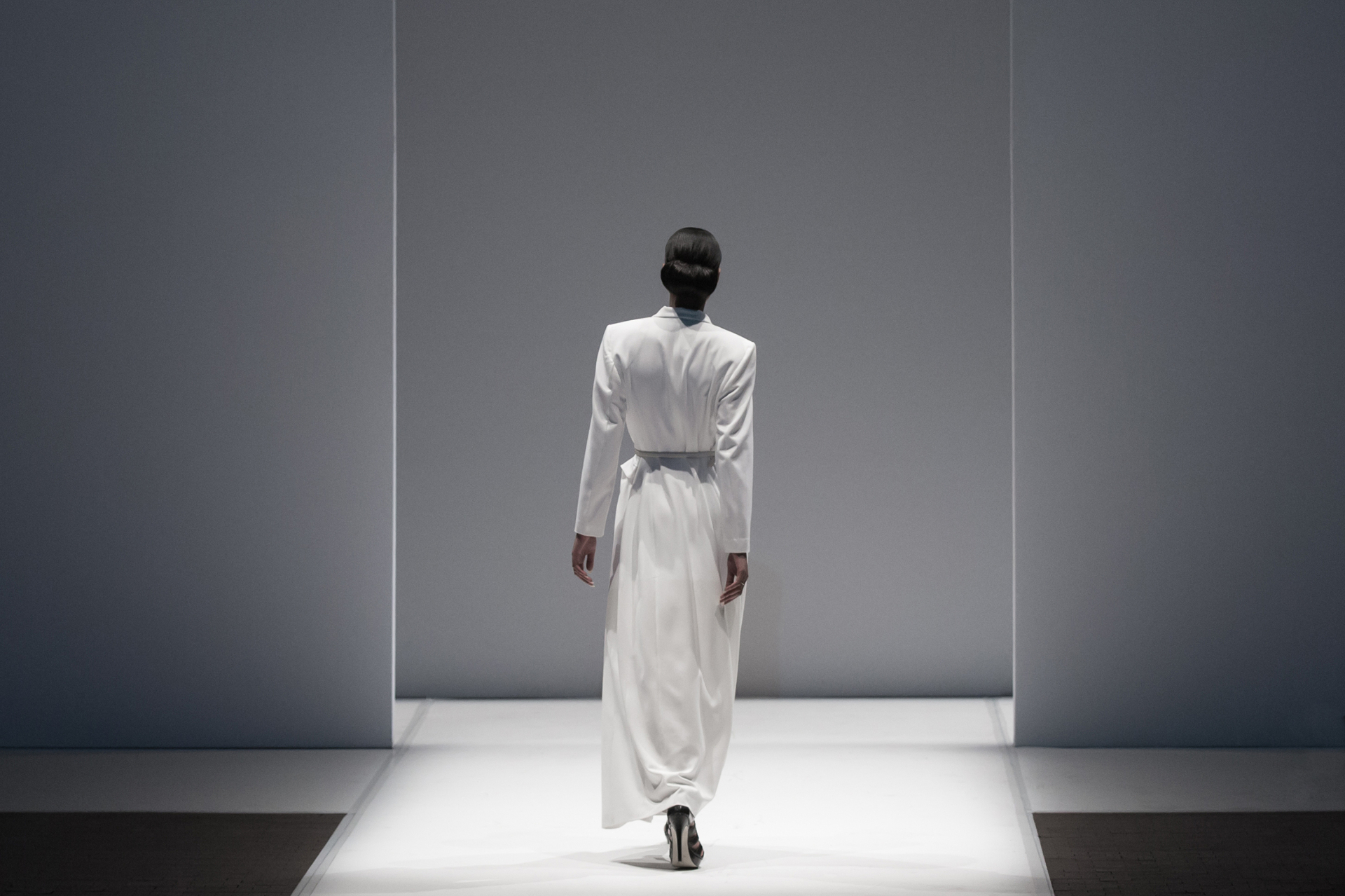Model in a flowing white garment walking a minimalist runway